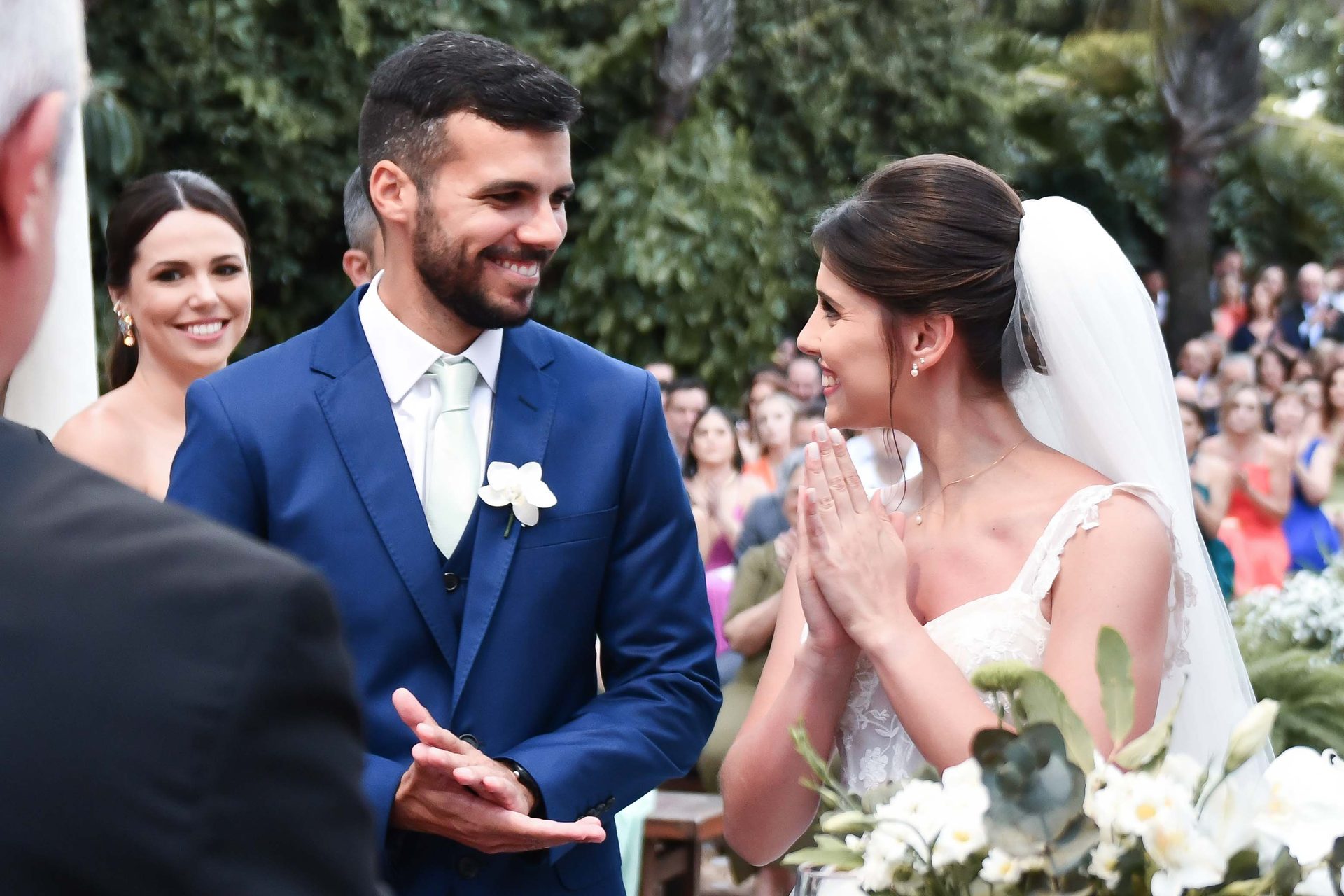 Noiva emocionada de mãos postas diante do noivo durante a cerimônia
