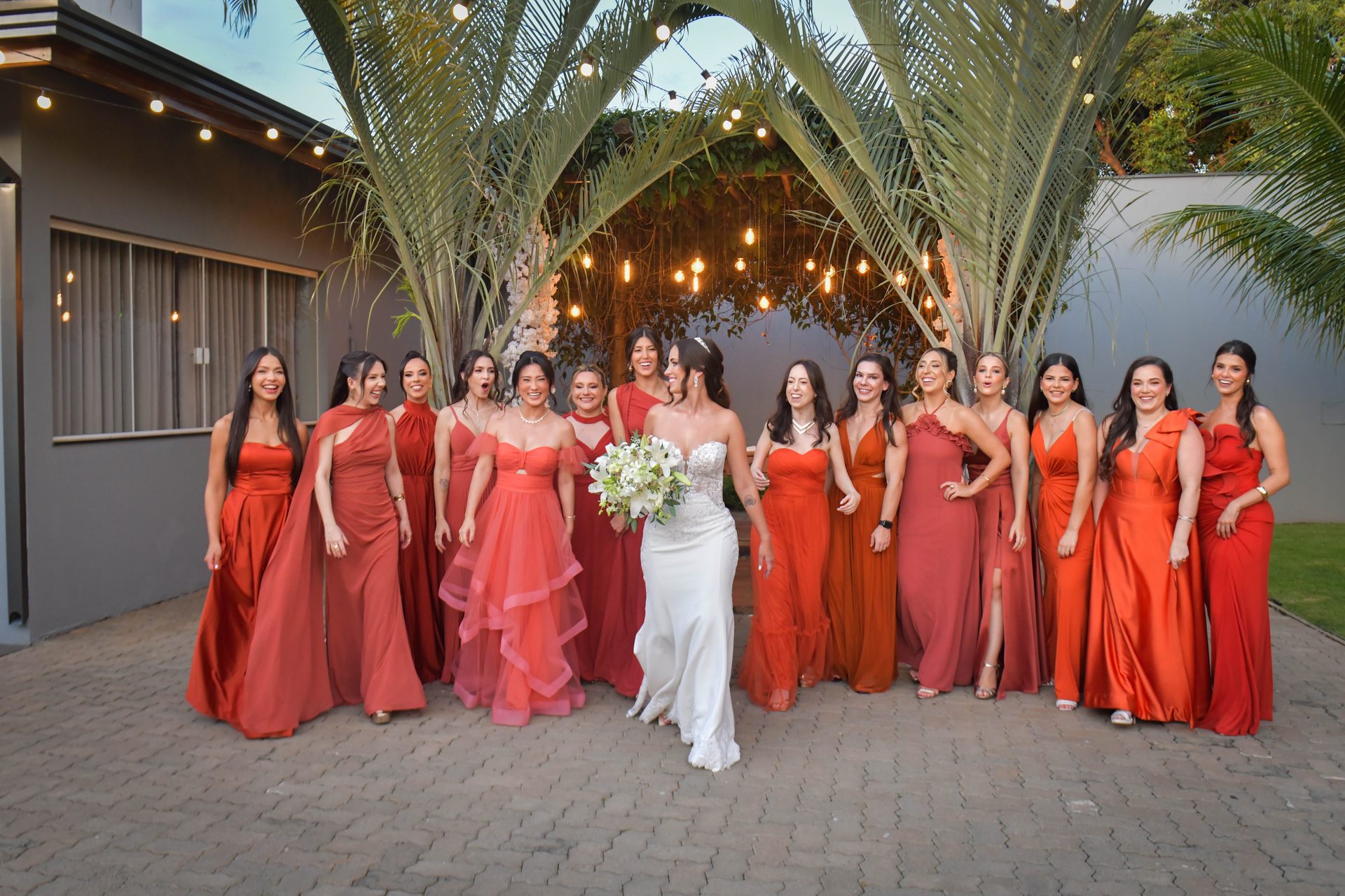Noiva ao lado das madrinhas em vestidos terracota sob luzes de festa