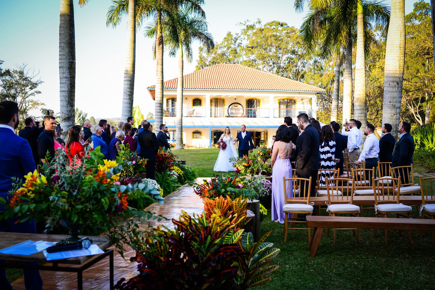 Cerimônia de casamento ao ar livre diante de casarão colonial cercado de palmeiras